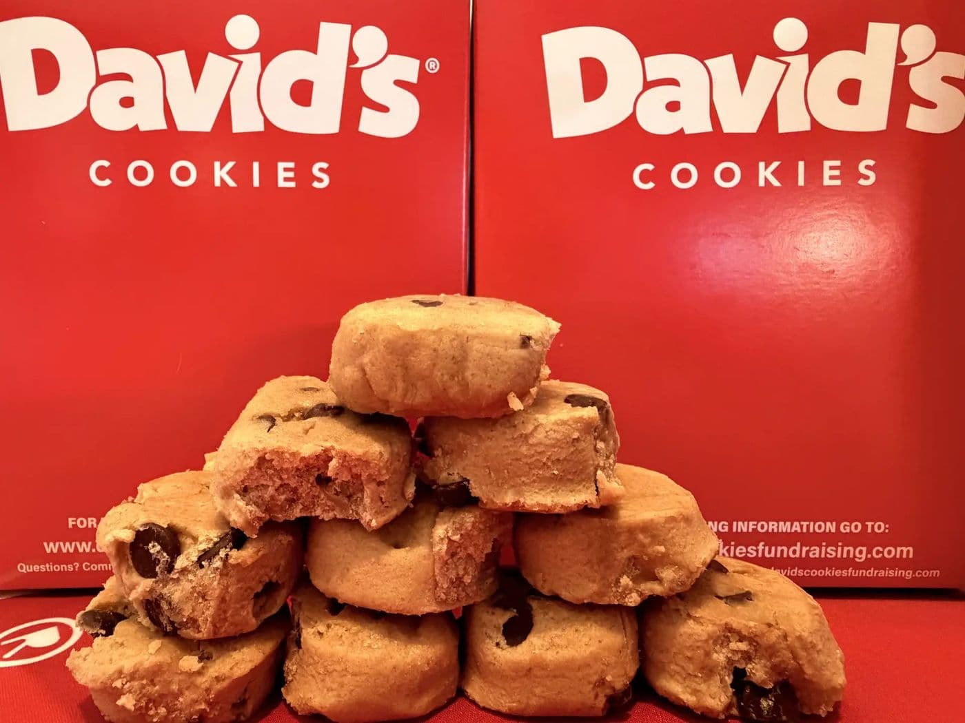 A stack of David's Cookies chocolate chip cookies in front of red David's Cookies boxes